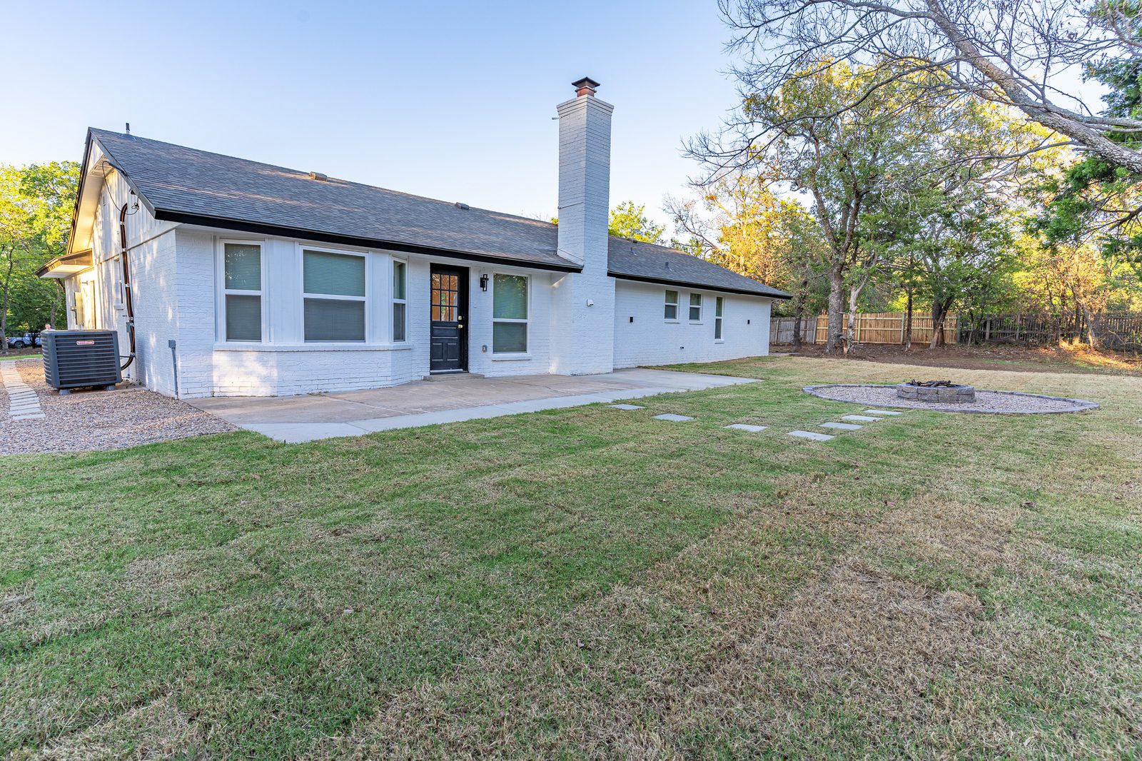 Backyard with patio, stepping stones and fire pit behind a white brick home, listing photo in Edmond, OK