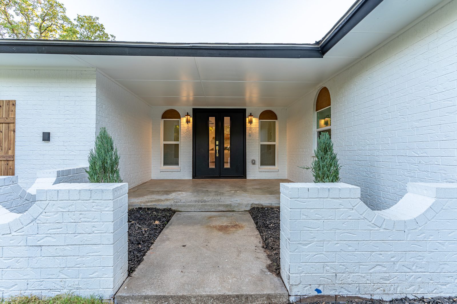 Covered front entry with black double doors and white brick planters, listing photo in Edmond, OK