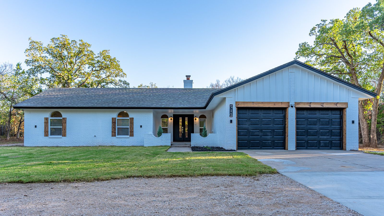 White brick ranch home with black garage doors and wood accents, front exterior listing photo in Edmond, OK