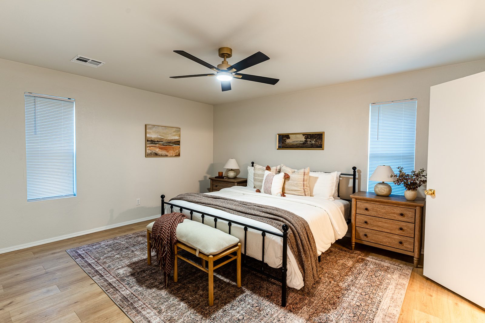 Staged primary bedroom with iron bed, wood nightstands and ceiling fan, listing photo in Edmond, OK