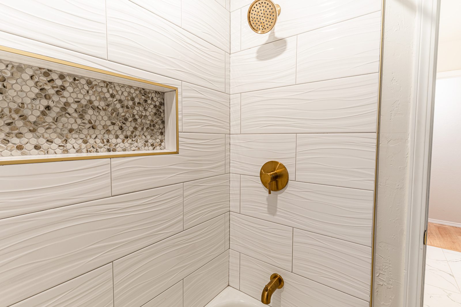 Shower detail with white wave tile, pebble niche and brushed-gold fixtures, listing photo in Edmond, OK