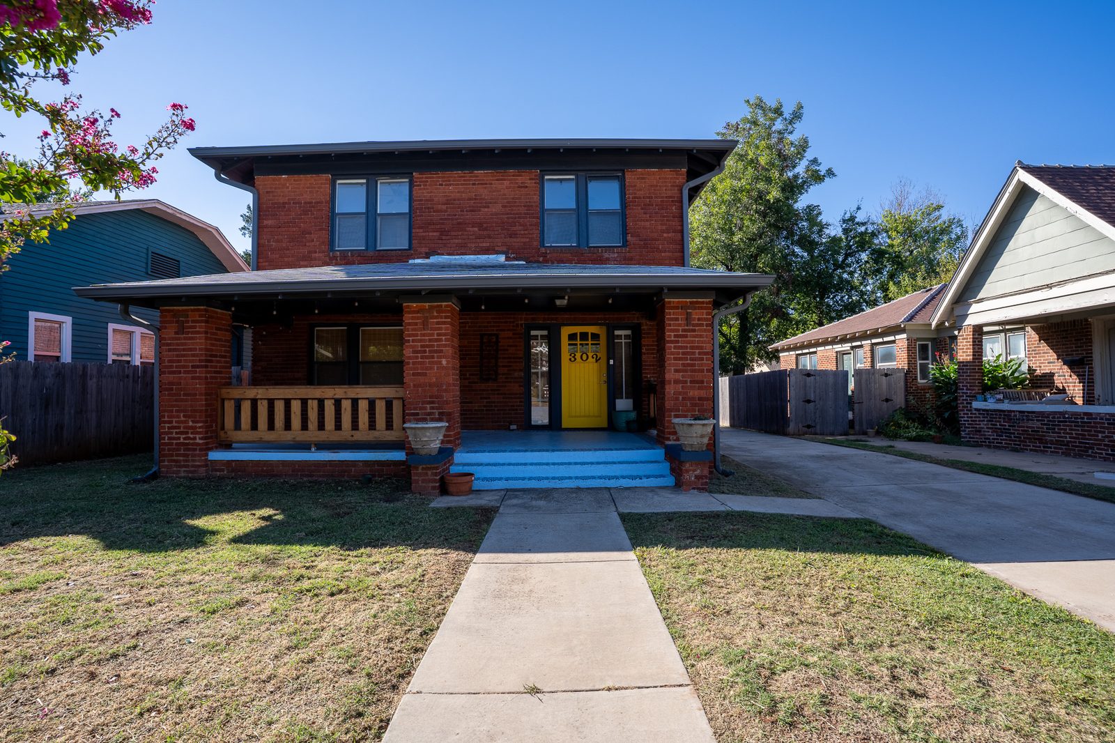Red brick two-story home with covered porch and yellow front door, listing photo in Oklahoma City, OK