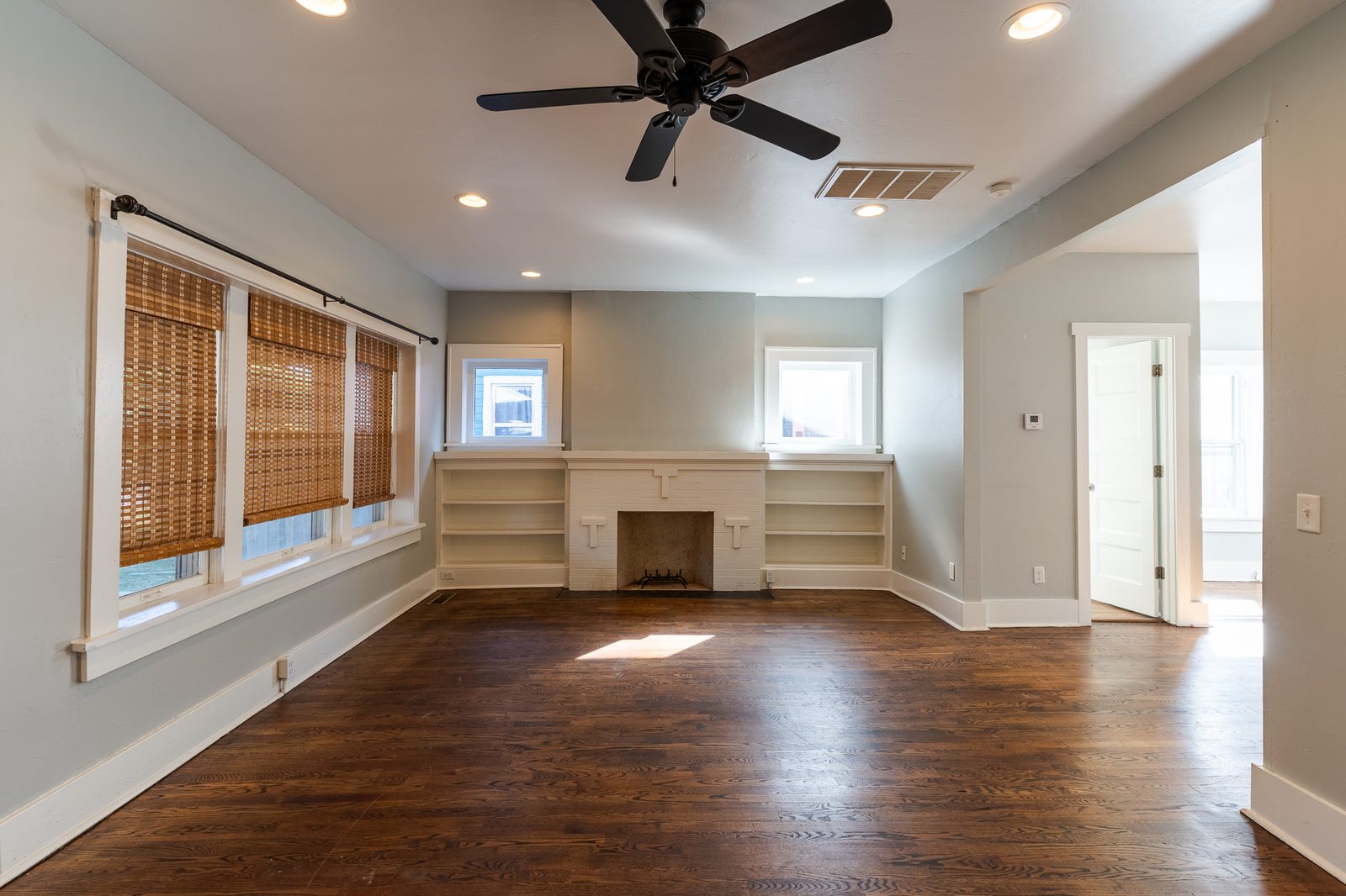 Vacant living room with hardwood floors, brick fireplace and built-in shelves, listing photo in Oklahoma City, OK